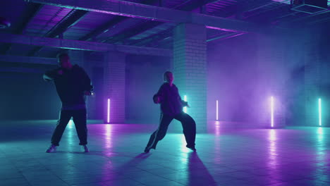 duet-of-young-male-and-female-dancing-hip-hop-street-dancing-in-the-studio-on-black-background.-Young-dancers-practicing-dance-routine-at-night-with-neon-lights.-Professional-dancers-dancing-hip-hop