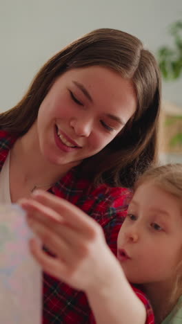 long haired young nanny with funny little girl looks at handmade picture in ebru art style in apartment slow motion. turkish design technique for family