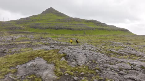 dos excursionistas caminan en un paisaje verde escarpado con terreno rocoso, exudando aventura