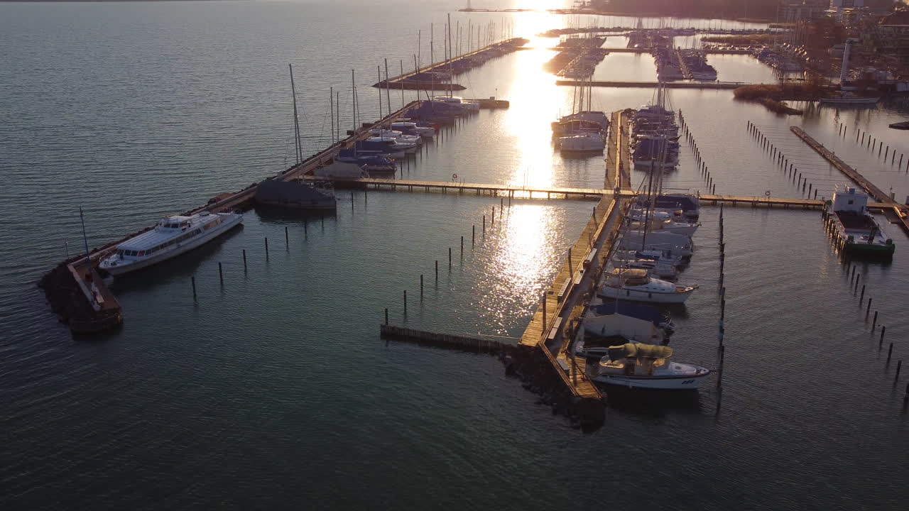 Aerial tracking shot of Balatonfured dock stretching into water with dramatic sunset colors