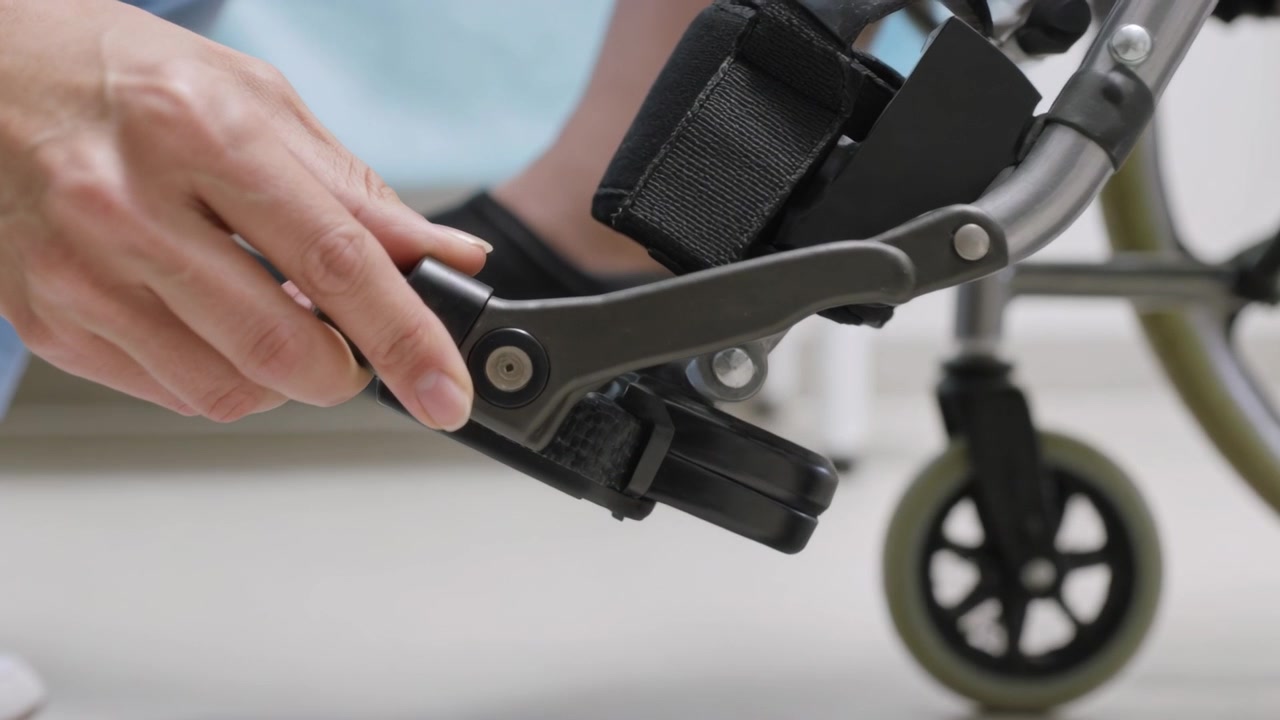 Approaching fingers as aide hand in scrubs grasping lever, securing strap to fasten foot at clinic