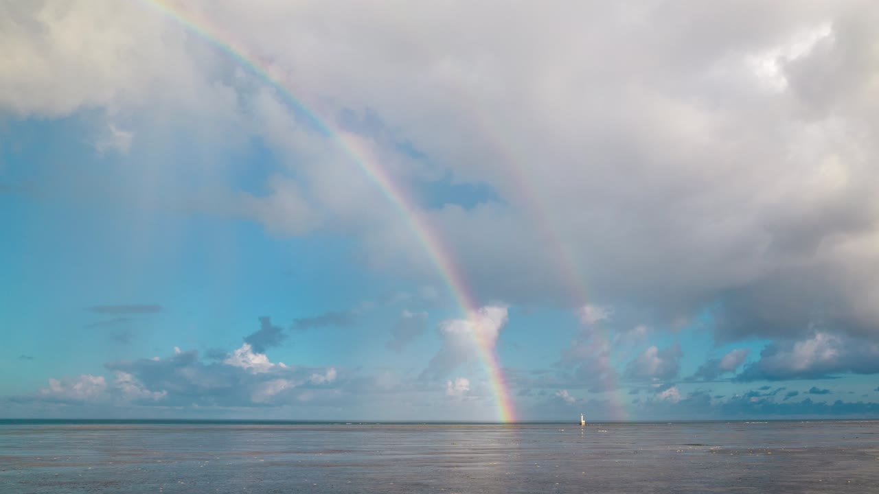 Double rainbows visible in sky above sea, after the dynamic movement of clouds. Time lapse.