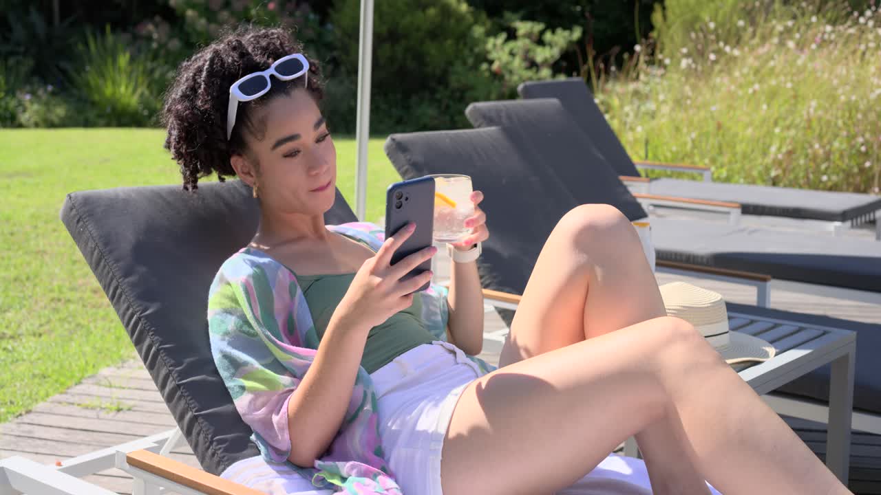 Donna che si rilassa su una sedia a sdraio sul ponte con un top da bagno verde, leggendo lo smartphone e sorseggiando una bevanda