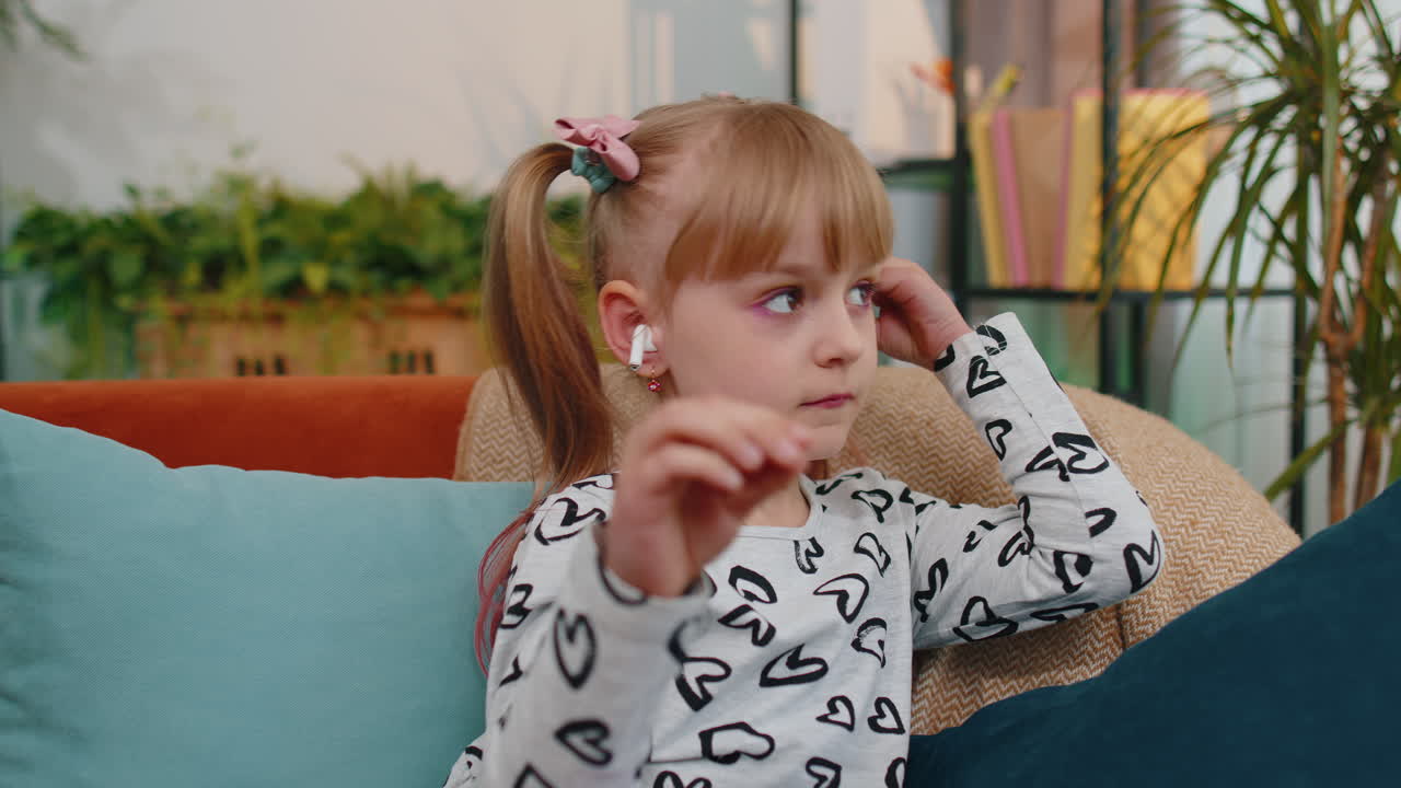 Una bambina piccola si rilassa sul divano, indossando auricolari wireless e ascoltando la sua canzone preferita.