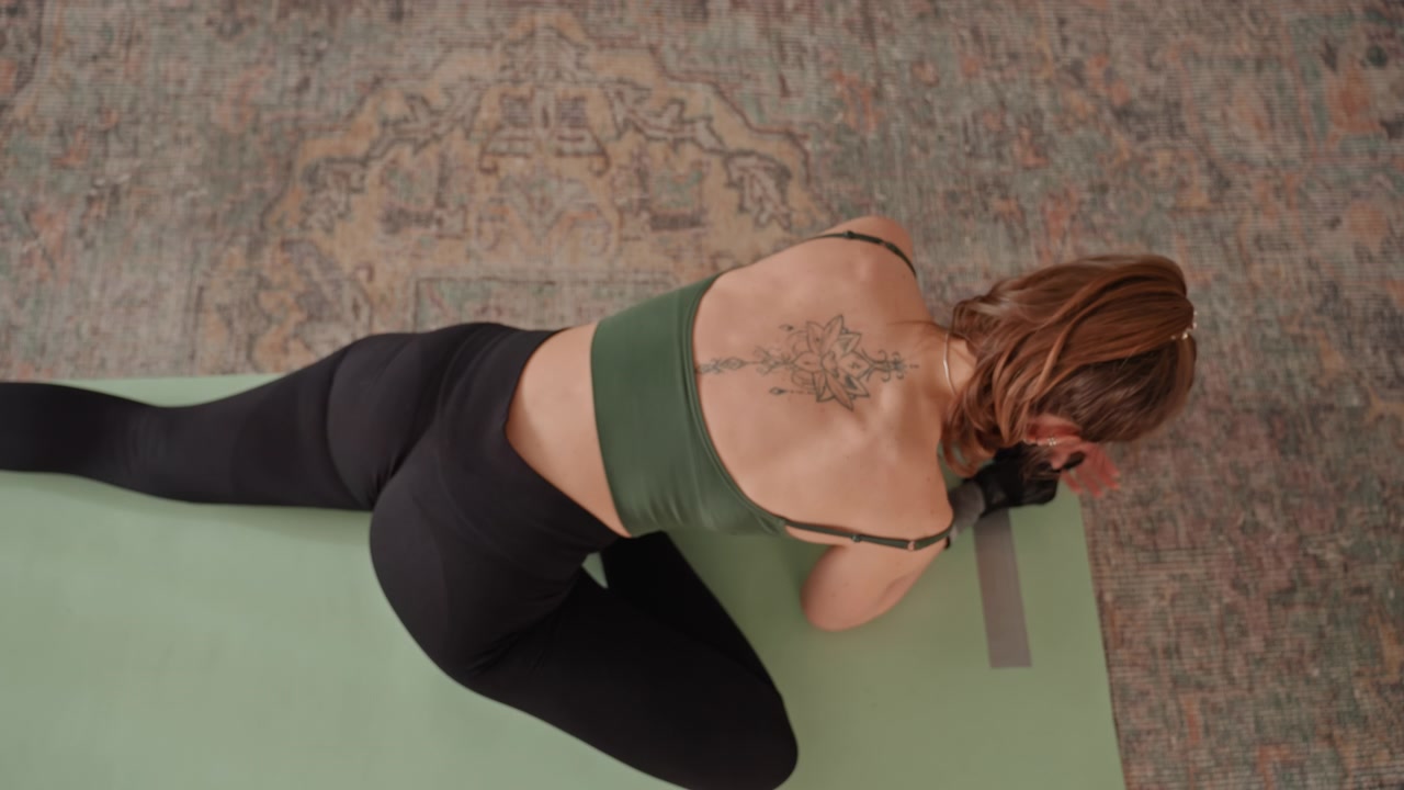 Woman performs hip stretch indoors. Female individual engaged in targeted hip stretching routine at home. Woman is diligently performing hip stretch exercise on green mat in her living room