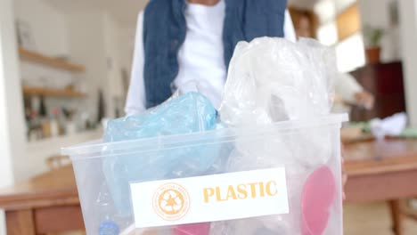 portrait of happy african american boy holding recycling box in kitchen, slow motion