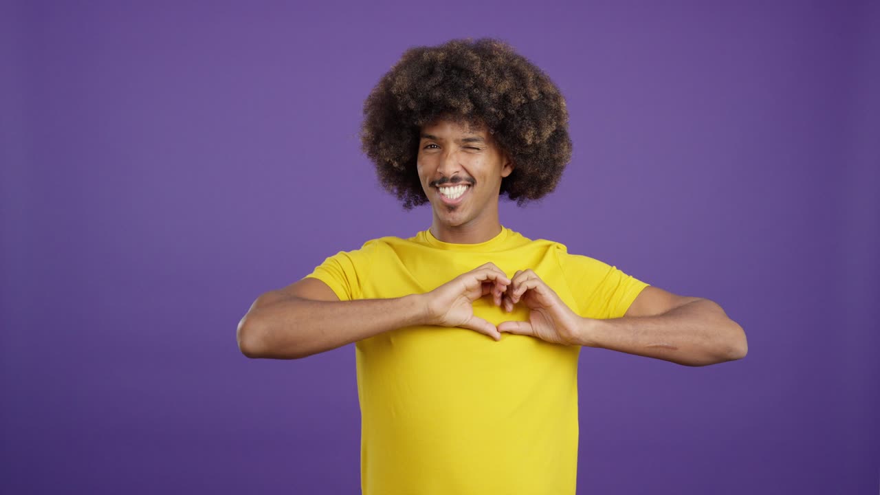 Man with afro and mustache posing and gesturing in yellow t-shirt on purple background