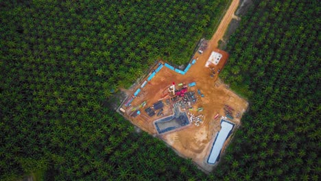 cinematic 4k drone footage of onshore drilling rig equipment structure for oil exploration and exploitation in the middle of jungle surrounded by palm oil trees during sunset and high oil price