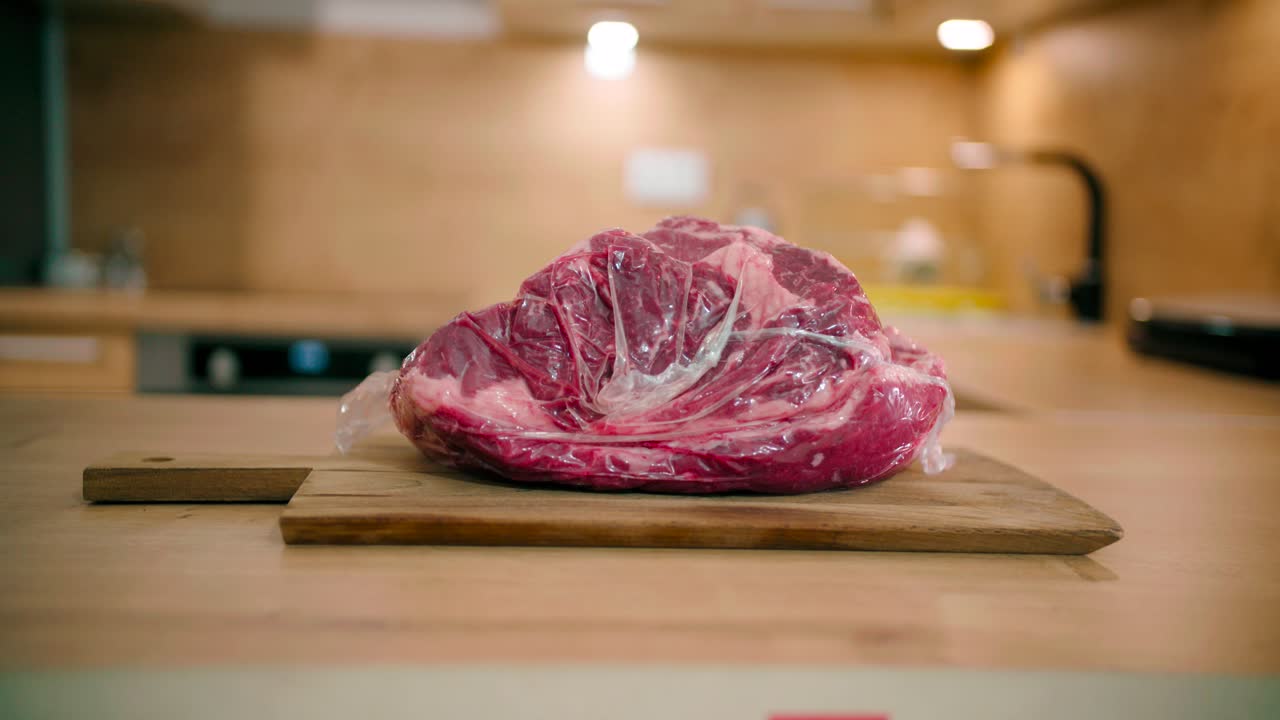 Primo piano di un uomo che posiziona una bistecca congelata confezionata su un tagliere di legno.