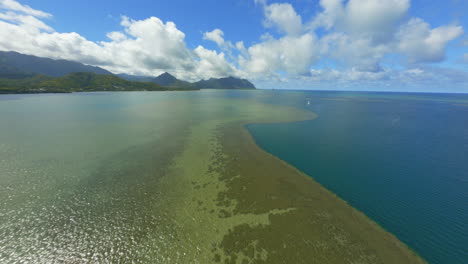 flying over kaneohe bay oahu hawaii, with mountains and clouds in background, gorgeous reef and water below