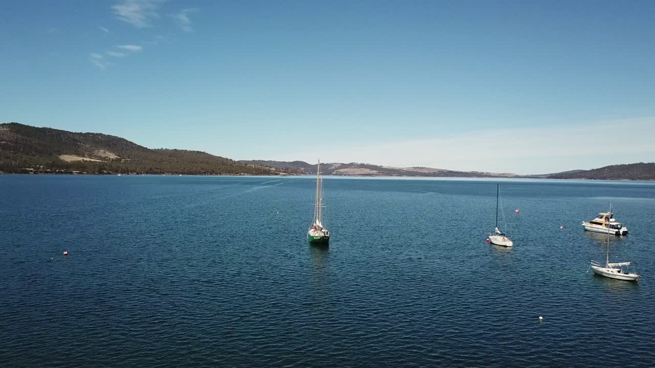 panorámica de drones aéreos sobre yates estacionarios en un mar azul profundo rodeado por una pequeña cadena montañosa de un día claro y soleado
