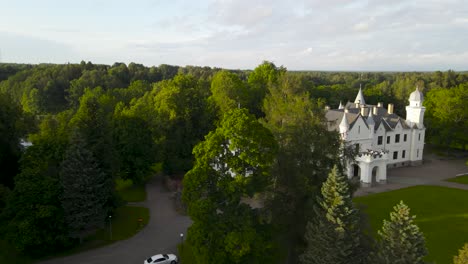 gorgeous aerial drone video of a large and spectacular white colored alatskivi castle during sunset. drone goes higher and reveals a large lake, forest and the tall towers of the building