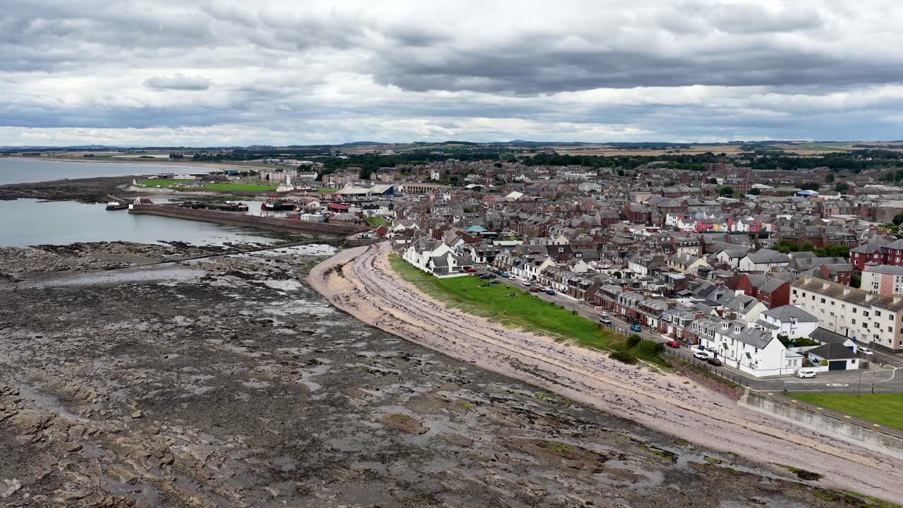 Drone pans above Dundee’s rocky coast, revealing town, harbor, cloudy sky, and North Sea