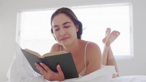 mujer caucásica feliz relajándose, acostada en la cama y leyendo un libro
