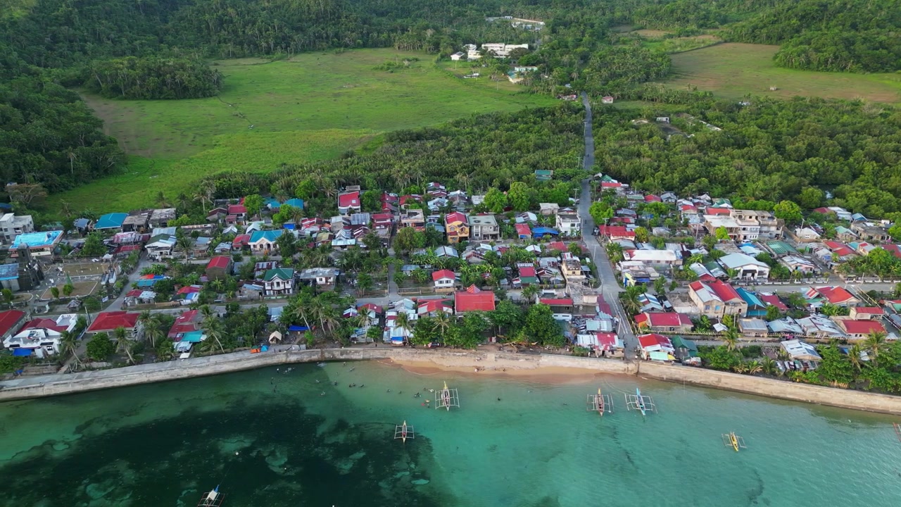 Virac, Catanduanes'teki kıyı şeridinde yer alan bir barangayın havadan yanal takip çekimi, sahil evlerini, bangka teknelerini ve tropikal yeşillikleri gösteriyor