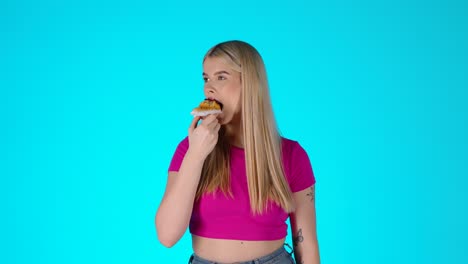young blonde woman enjoying eating muffin pastry, colorful studio portrait