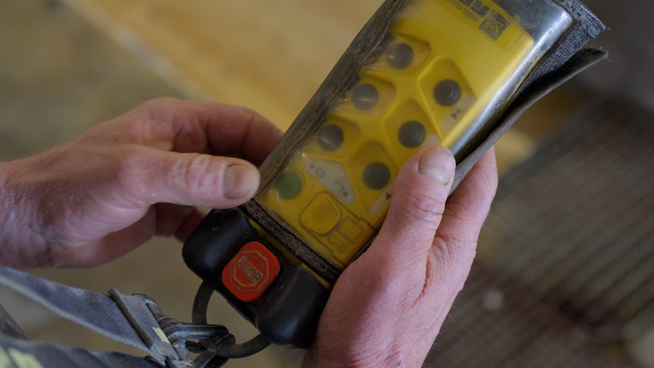 A male worker holds a yellow remote control in his hands, featuring buttons and a stop button