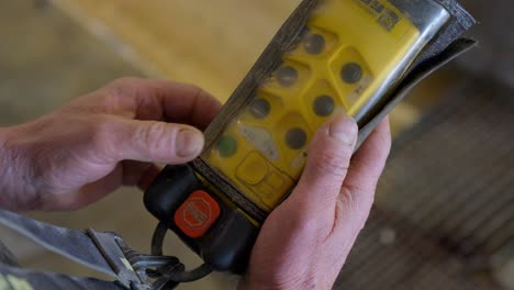 A-male-worker-holds-a-yellow-remote-control-in-his-hands,-featuring-buttons-and-a-stop-button