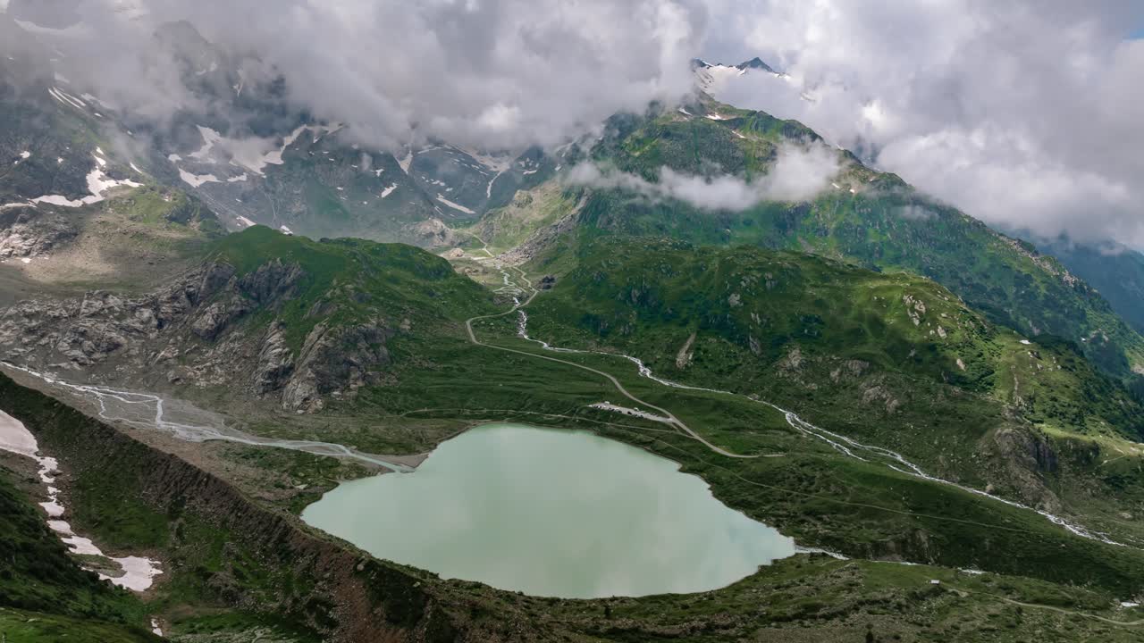 Aerial drone timelapse video of clouds rolling over a mountain lake in Sustenpass, Switzerland, showcasing serene alpine landscapes with dynamic weather changes and scenic views of peaks