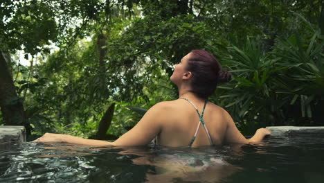 Young-Woman-in-swimsuit-views-jungle-foliage-from-hot-spring---tracking-medium-shot