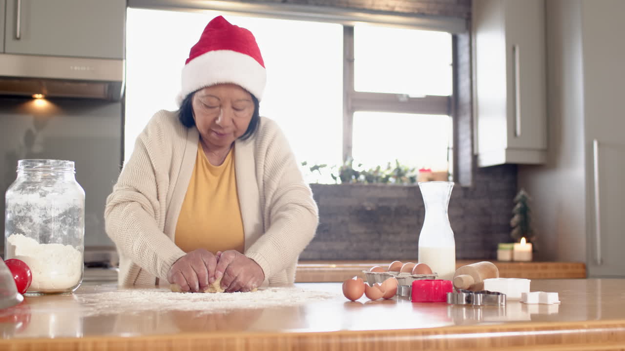 Elderly woman wearing Santa hat baking Christmas cookies in cozy kitchen