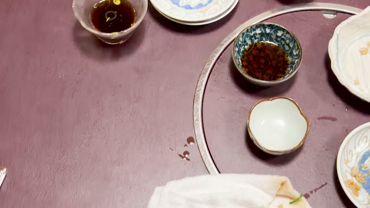 Overhead camera pans across a restaurant table with finished plates, soy sauce, and used towels