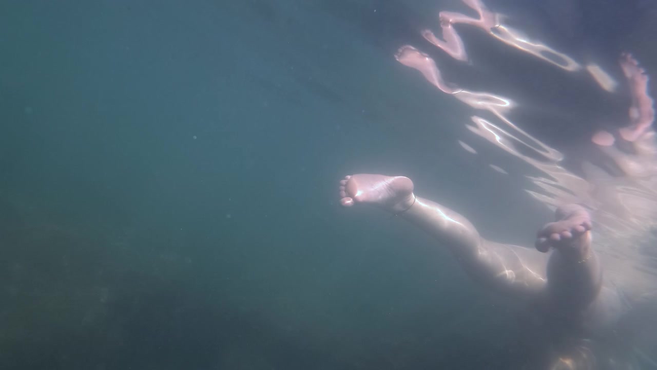 Person swimming underwater, a foot and lower leg showing through the water's surface, sunlight reflecting on the ripples creating movement