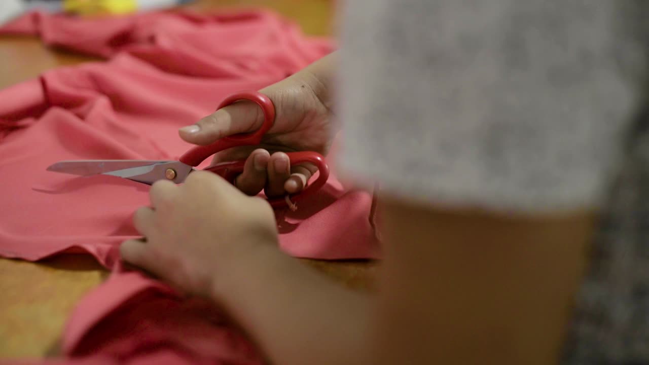 costurera latina cortando un vestido para más ajustes usando tijeras en el taller sobre una mesa de madera