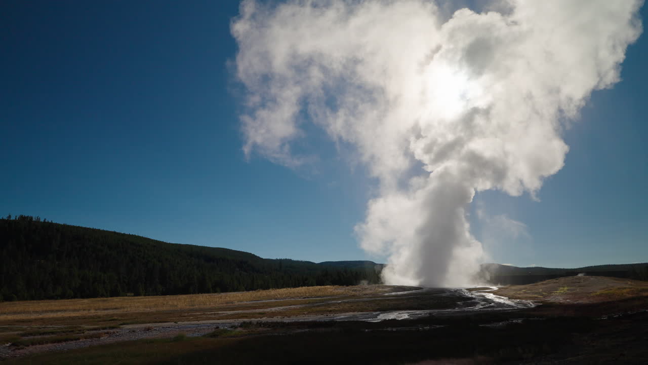 Geyser erupting with a large plume of steam under a blue sky