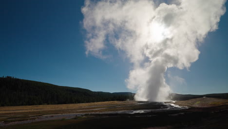 geyser erupting with a large plume of steam under a blue sky