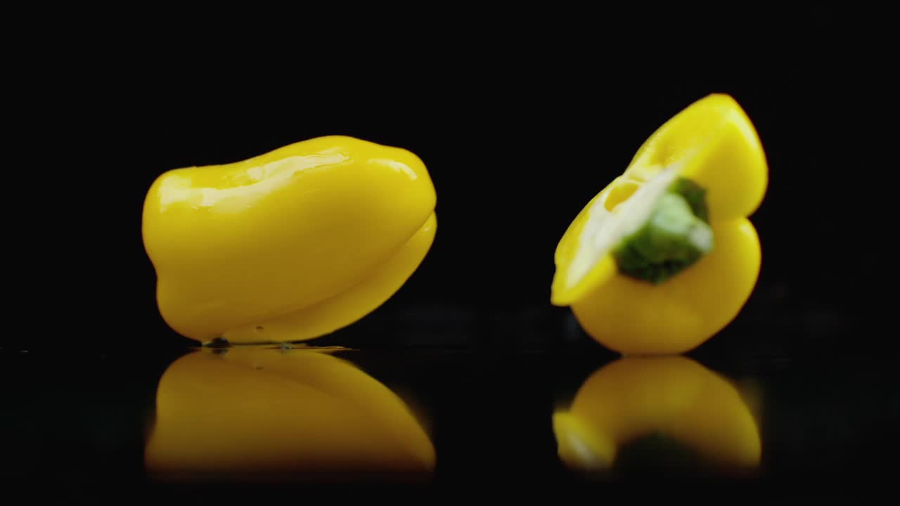 Yellow juicy cut bell pepper falling on glass with water splashes in slow motion on a dark background