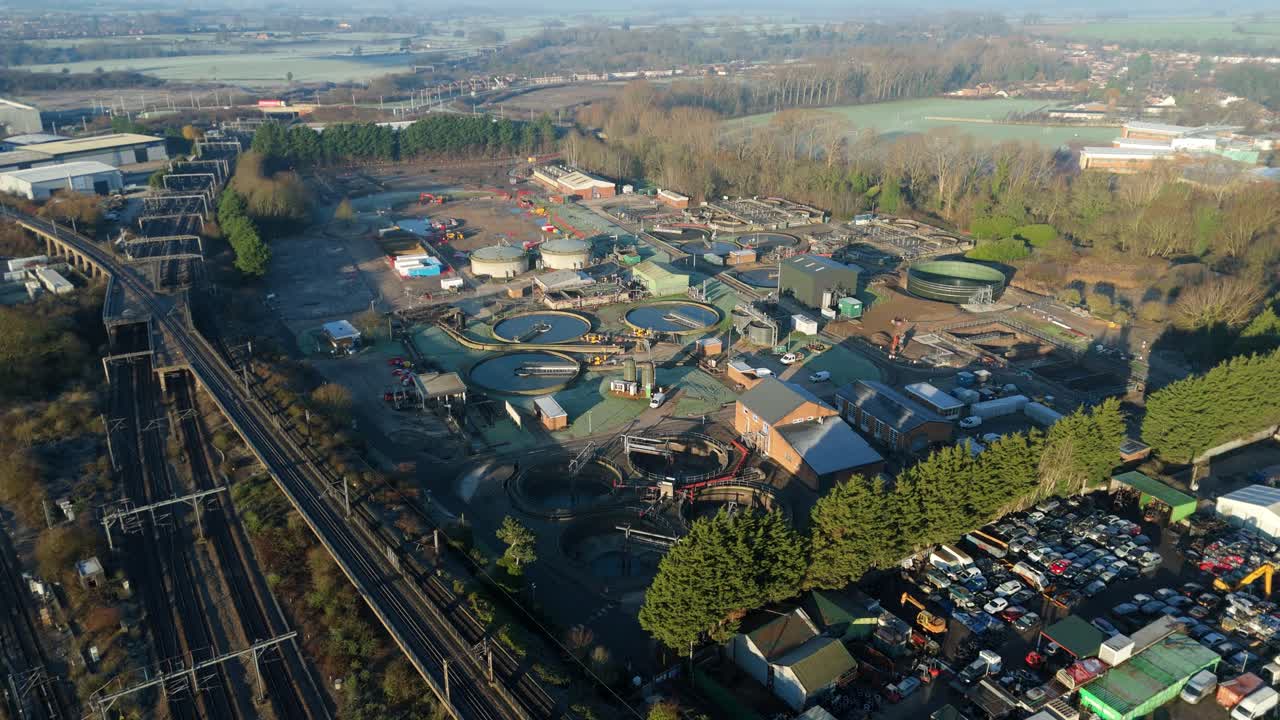 High-angle drone perspective of expansive manufacturing warehouses adjacent to a busy railway junction in Rugby England