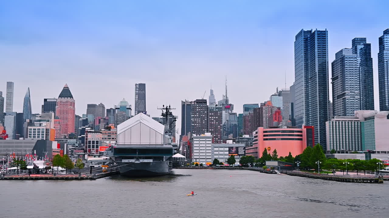 Diverse modern buildings at the waterfront of New York, USA. An amphibious transport dock ship of the United States Navy at the berth