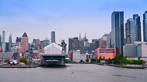 diverse modern buildings at the waterfront of new york, usa. an amphibious transport dock ship of the united states navy at the berth