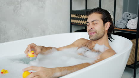 man relaxing in a bubble bath with rubber ducks