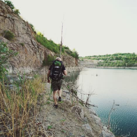 tourist with a backpack is going along the bank of the river on the background of rocks and wild nature in the summer.