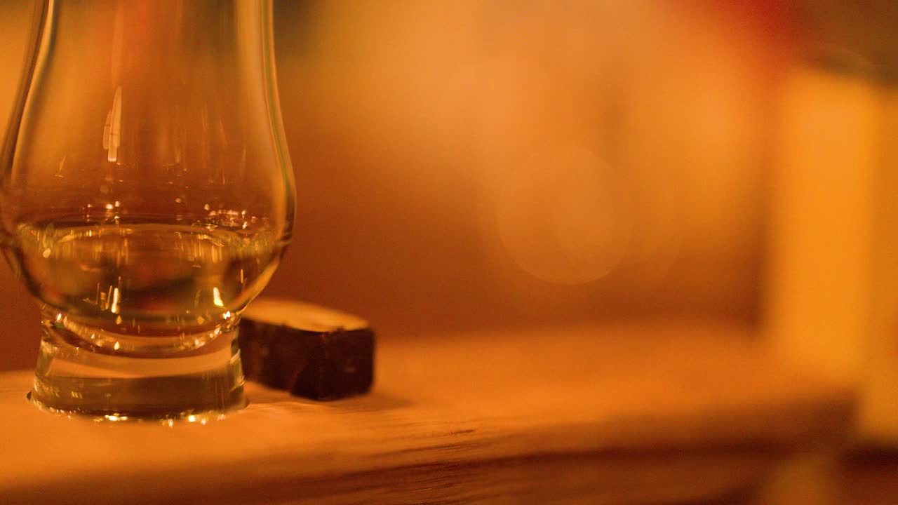 Close-up of whisky glass and chocolate piece on wood, warm ambient lighting, shallow focus
