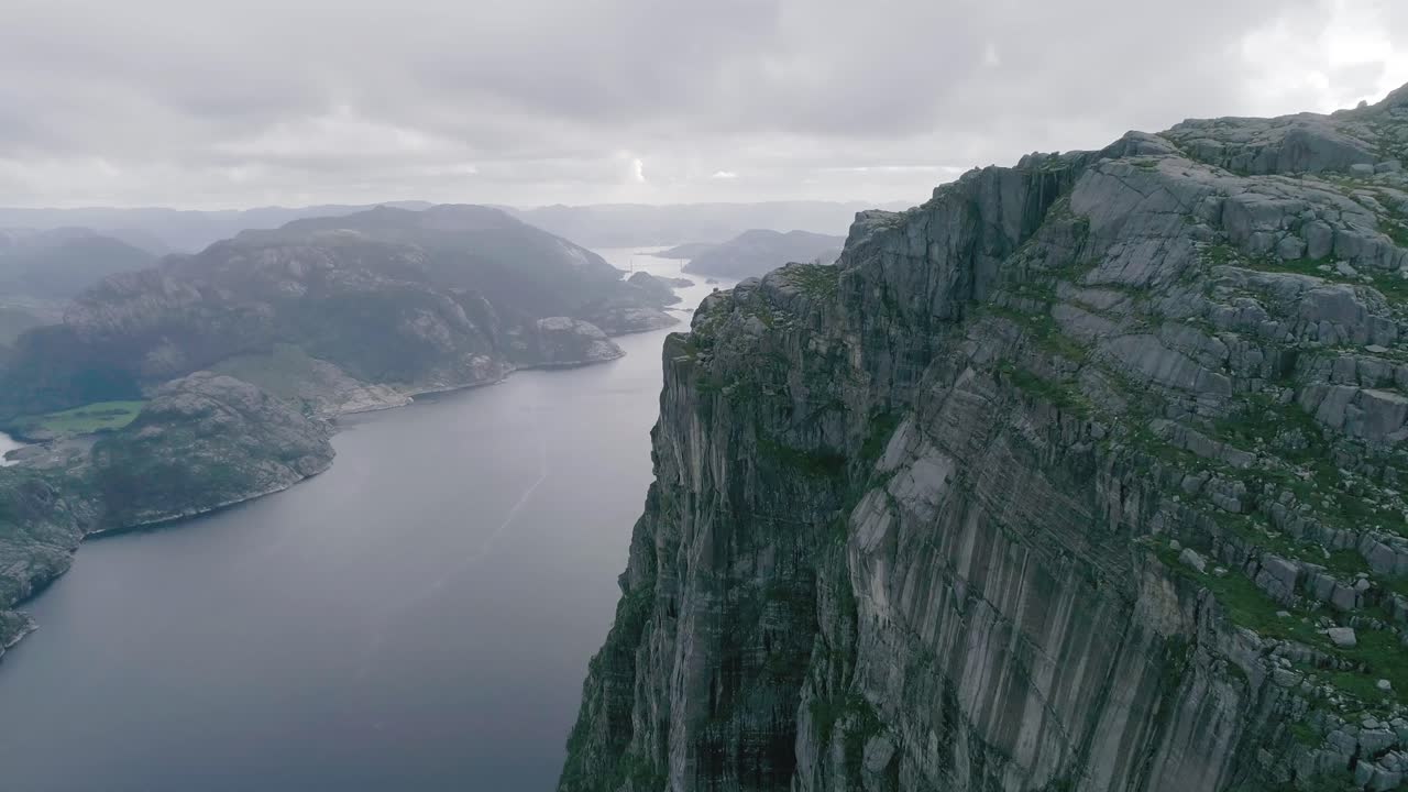 Luftfoto i slowmotion af norske fjelde, der afslører en fjord og en stor bro i baggrunden, under overskyet vejr.