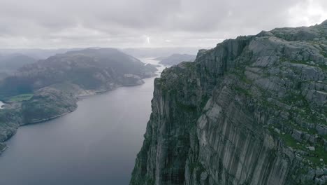 Toma-Aérea-En-Cámara-Lenta-De-Las-Montañas-Noruegas,-Revelando-Un-Fiordo-Y-Un-Gran-Puente-En-El-Fondo,-Durante-El-Tiempo-Nublado