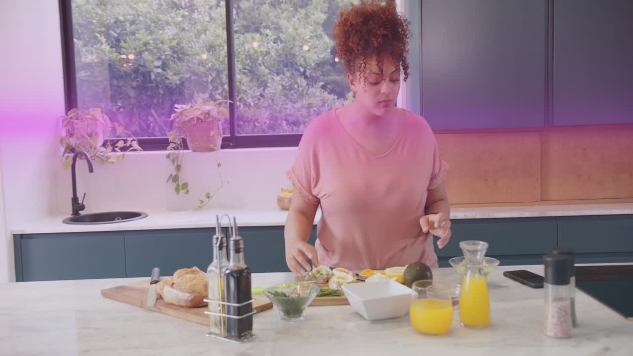Kvinde rækker ud efter en kniv, skærer avocado og topper toast på et bræt, farvebånd krydser madanretningen