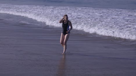 Middle-aged-white-woman-walking-out-of-Pacific-Ocean-in-Venice-Beach,-California-in-slow-motion