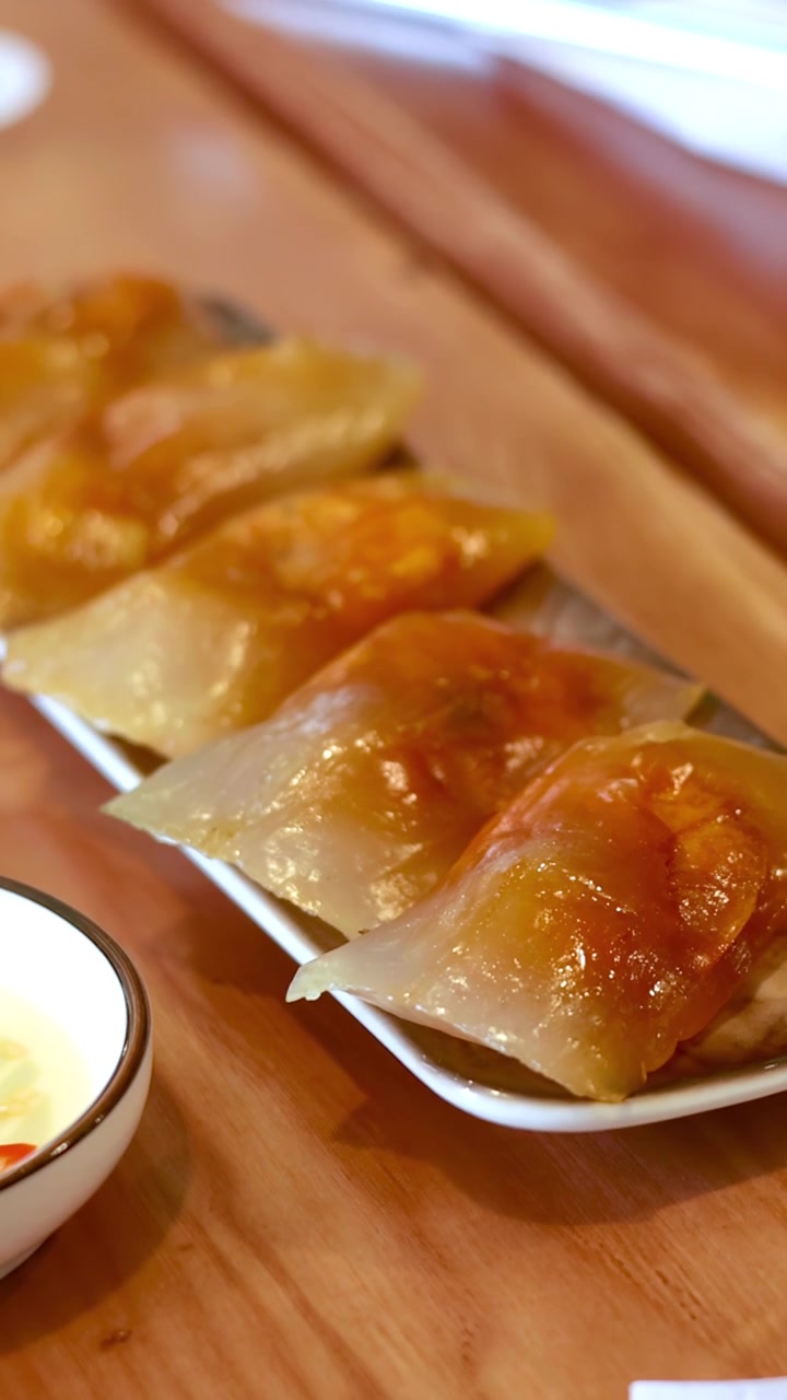 Close-up shot of translucent shrimp dumplings on a white plate with dipping sauce and chili