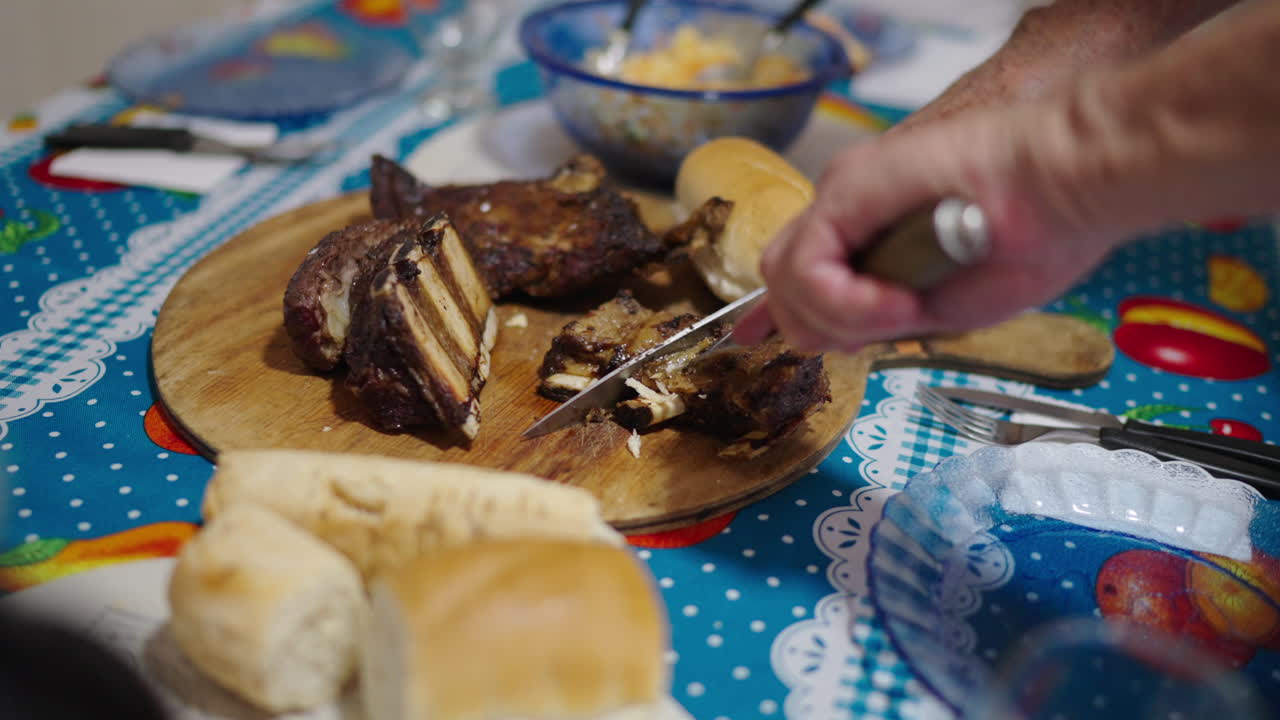 Grilled Argentine Ribs Being Sliced at Family Dinner Table with Bread and Homemade Sides