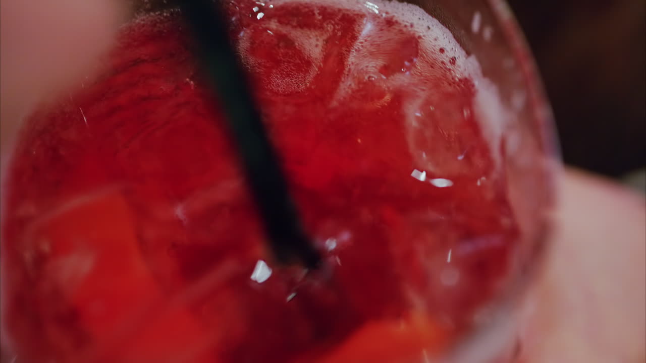 Close up of a woman mixing a red cocktail with a black straw