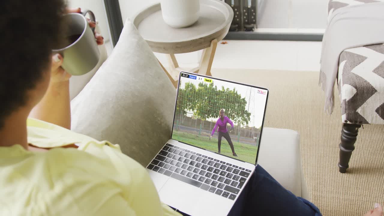 Video of person sitting on the couch and watching football match on laptop