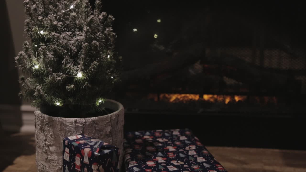 밤에 벽난로 근처의 나무 바닥에 놓인 냄비에 불빛이 있는 작은 크리스마스 트리 - 클로즈업 샷