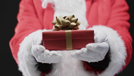 video of santa claus holding christmas present with copy space on black background