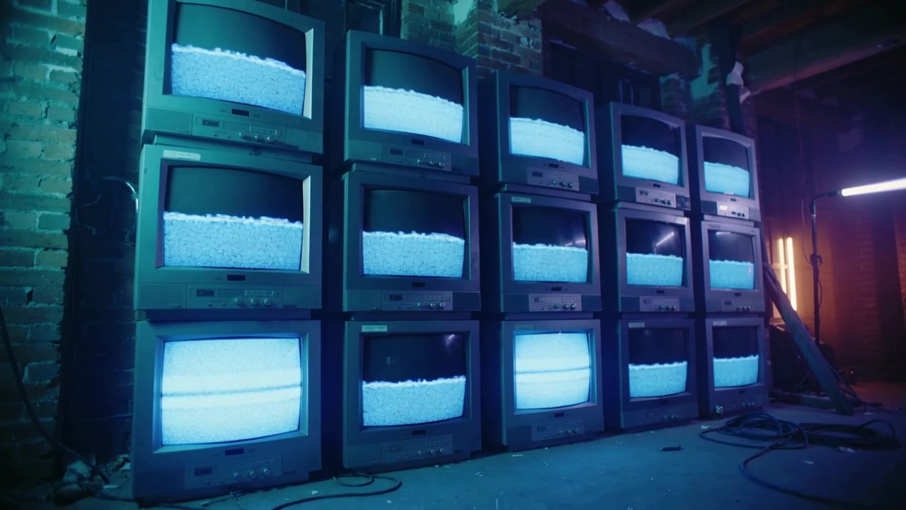 Powering stacked CRT bank displaying shifting cyan bands in dim warehouse with cables