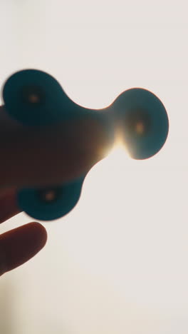cu shot: man hand silhouette playing with blue spinner against bright sun backlight near window in room extreme close view