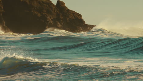 enormes olas rodando sobre la orilla durante la puesta de sol con acantilados escarpados en el fondo